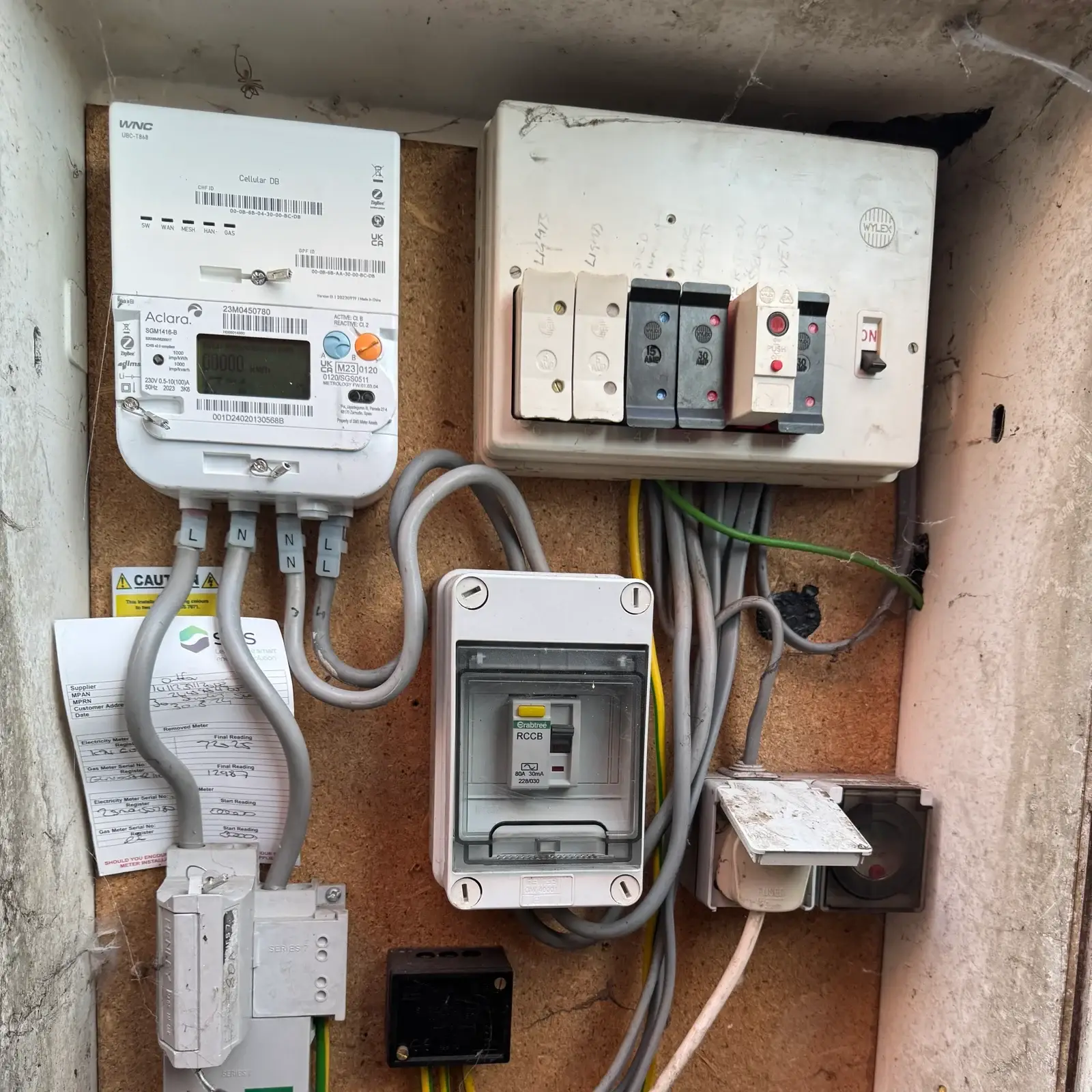 Old electrical consumer unit and meter setup inside cabinet